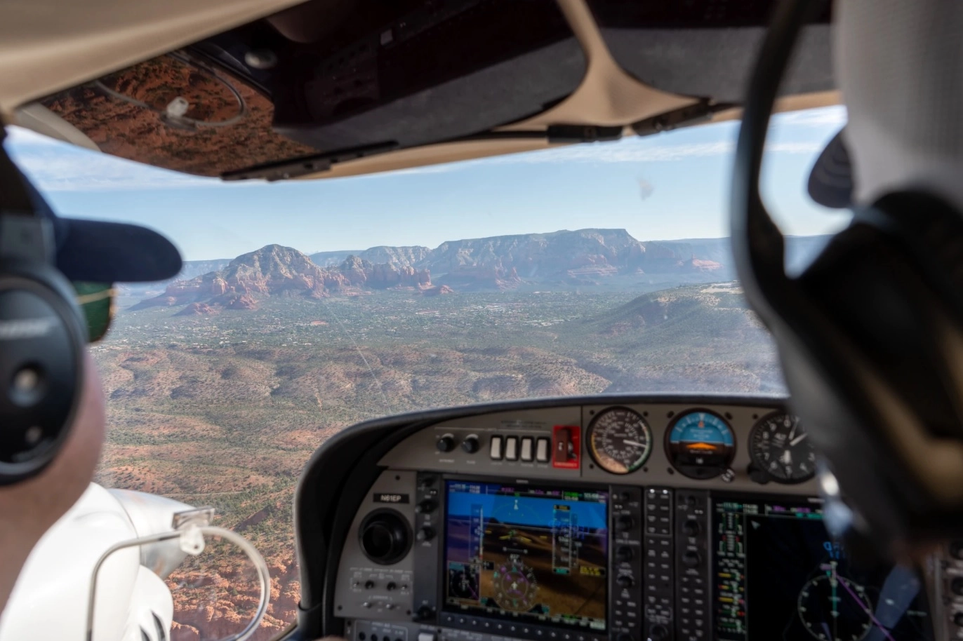 View from behind pilots in the cockpit of aircraft flying over land with mountains in sight