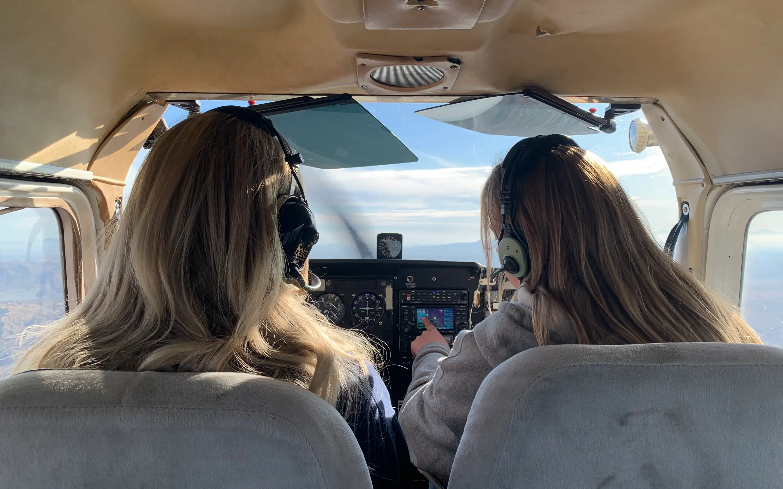 Over the shoulder view of two women pilots in cockpit of flying airplane