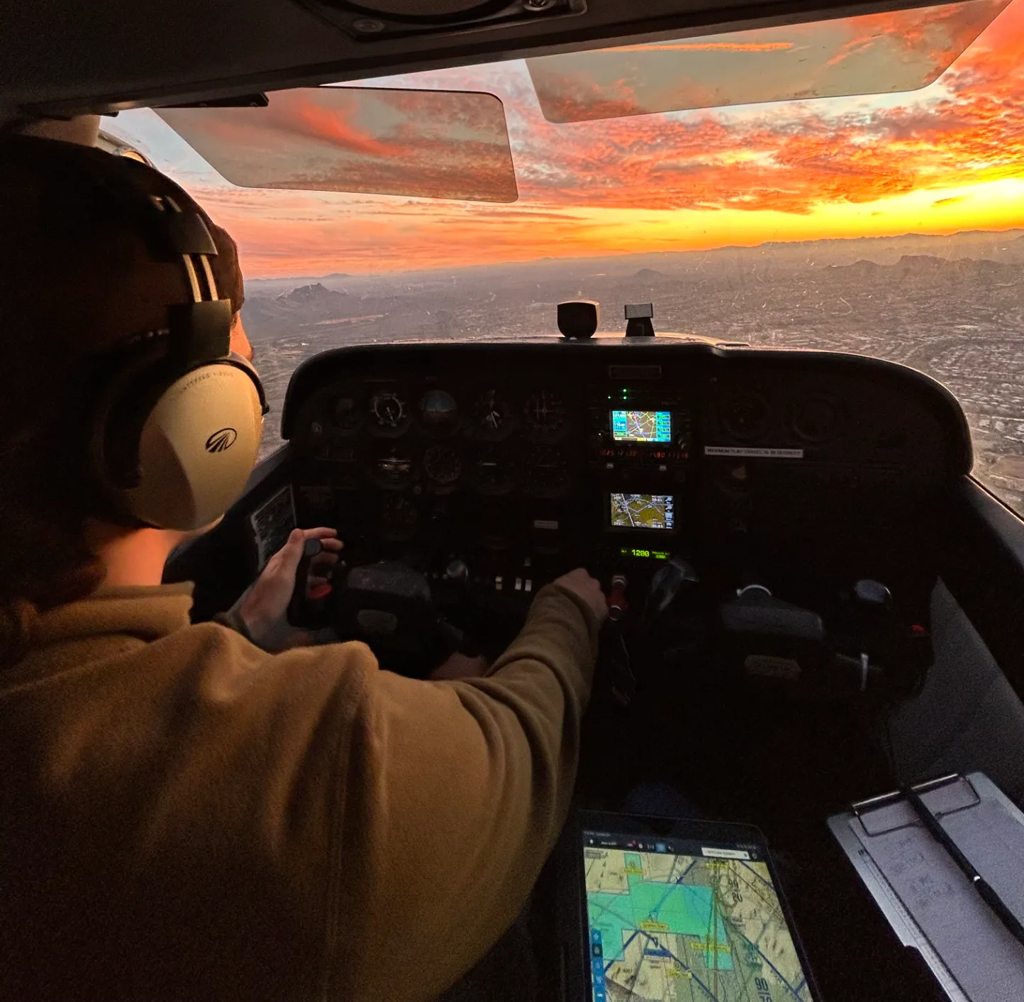 Pilot in aircraft cockpit seen from the back during flight with the sunset in the horizon