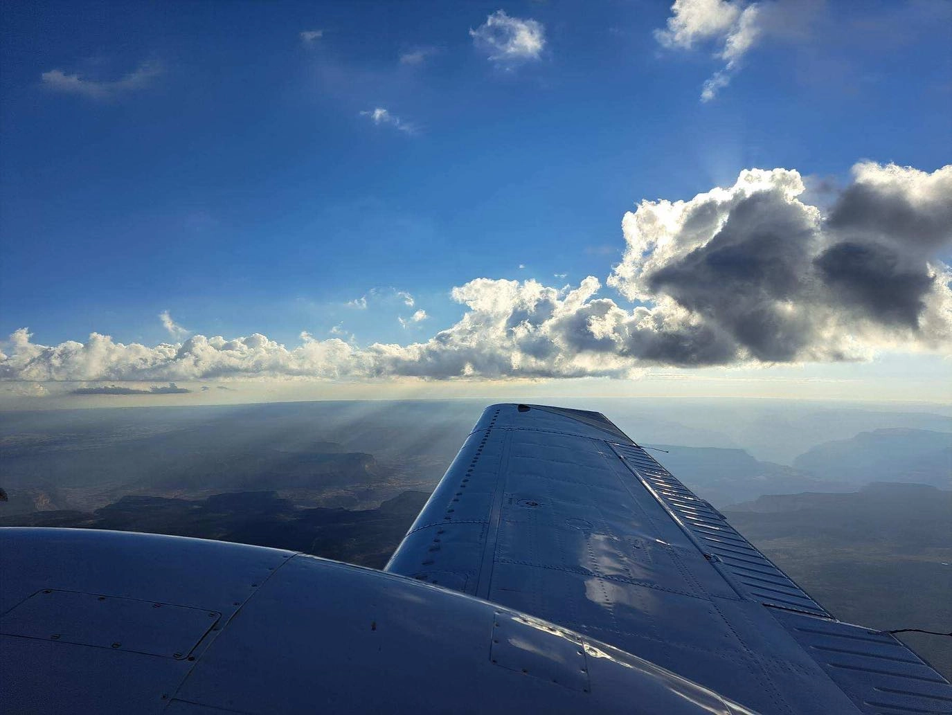 View of an airplane's wing during flight with a landscape below and clouds in the horizon