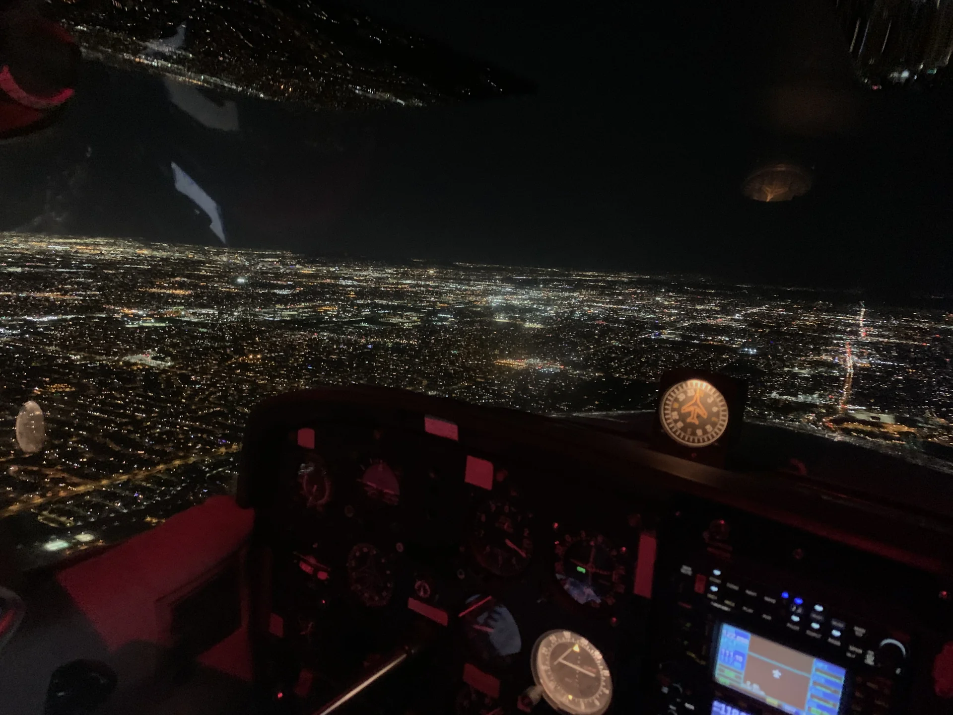 Red-lit Cessna instrument panel at night with the lights of the Phoenix metro spread out below